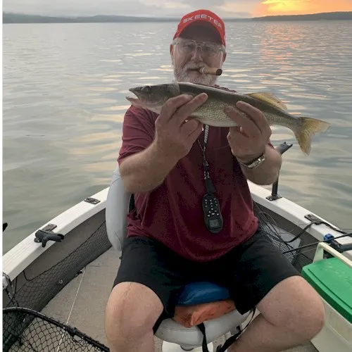 Man holding fish on boat at sunset